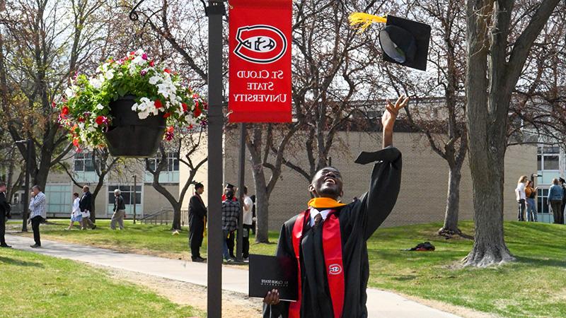 Student throwing graduation cap under a St. Cloud State University banner