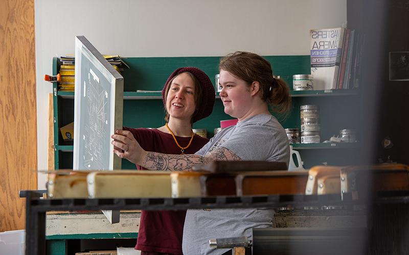 Student looking at artwork with teacher